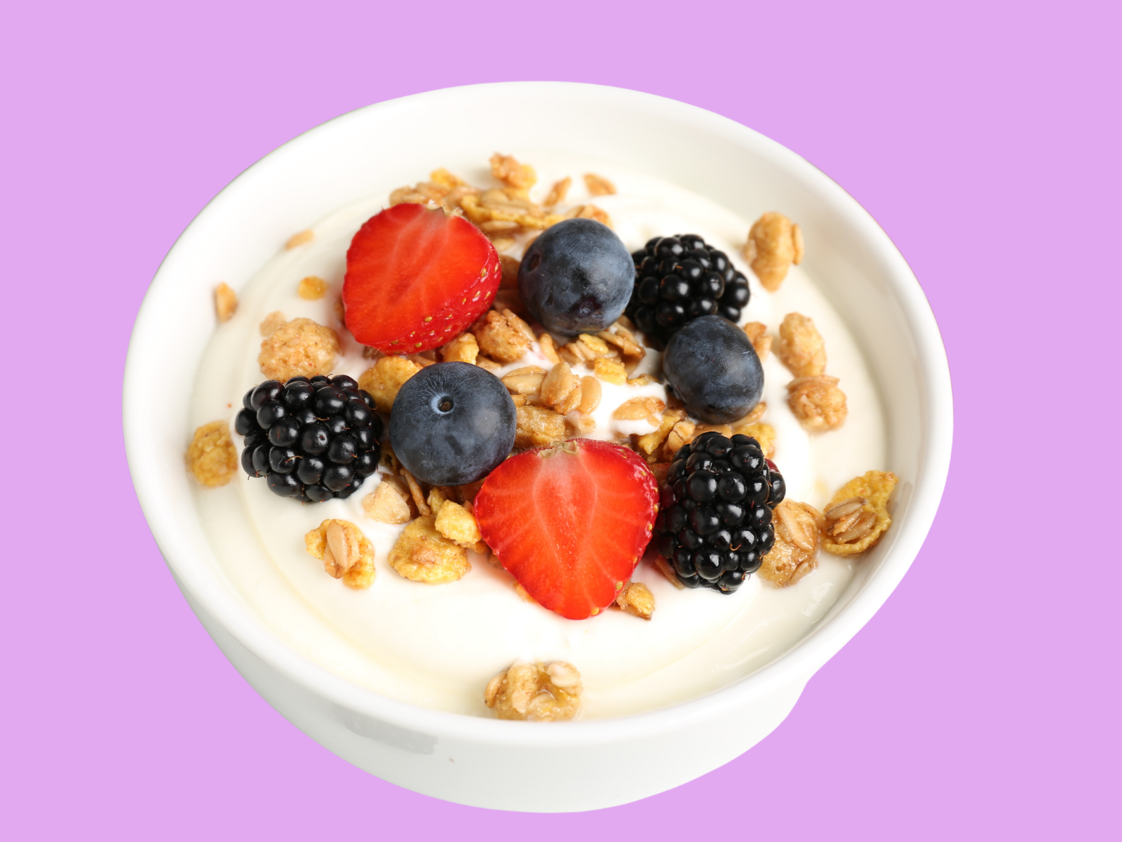 A white bowl of frozen yogurt topped with strawberry halves, blueberries, blackberries and granola
